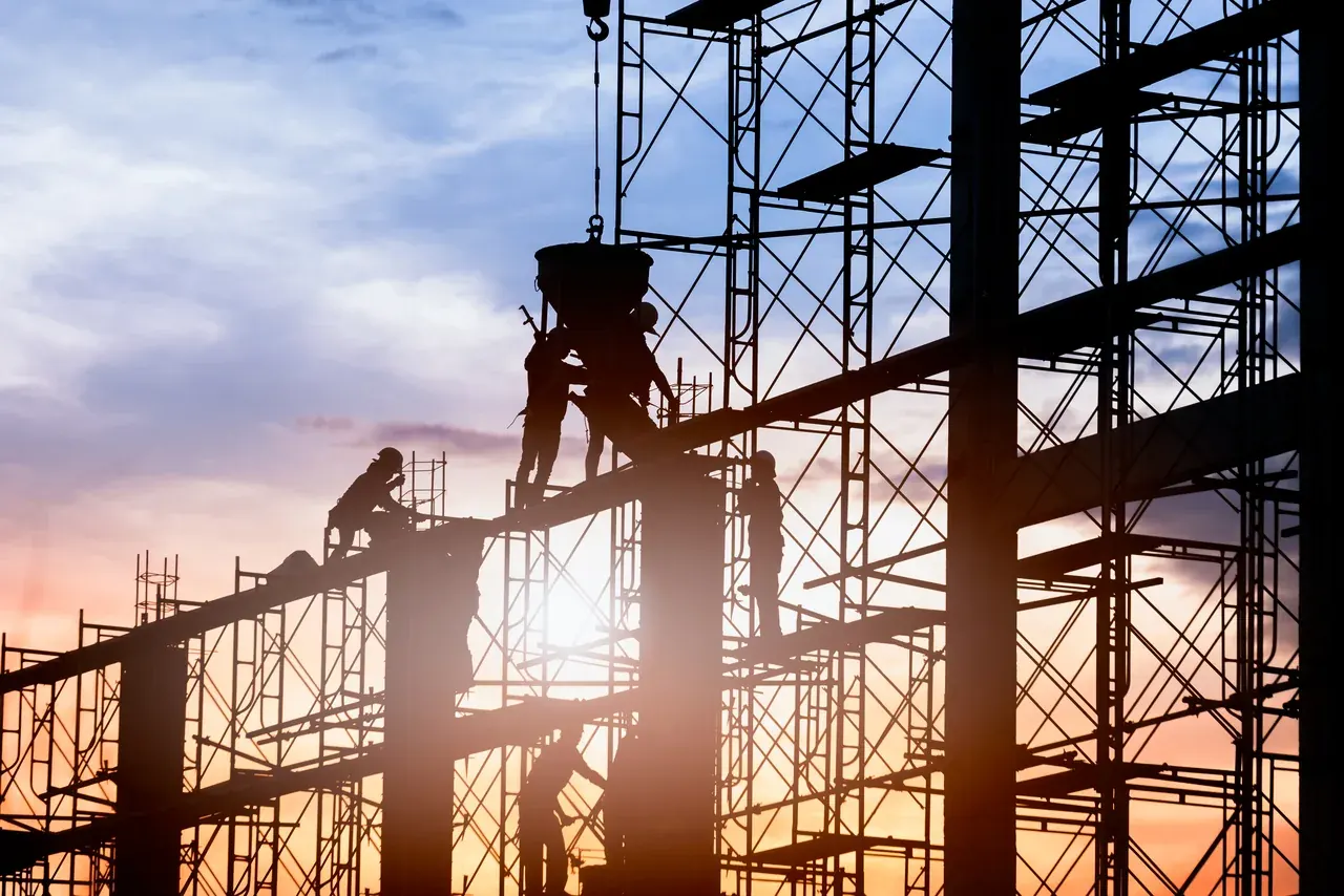 Operarios trabajando sobre la estructura de una obra a contraluz al atardecer